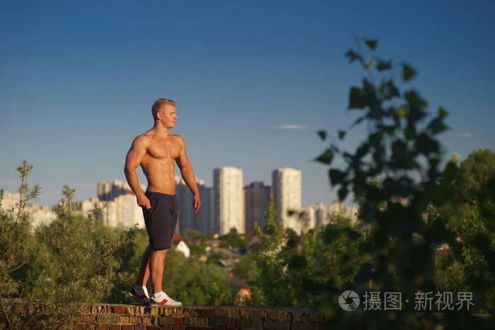Muscular young man standing on top of the roof and looking at du