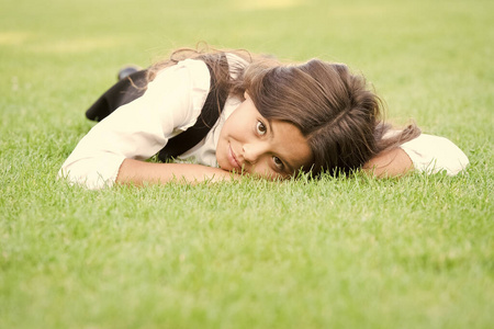 可爱放松的样子。可爱的女孩带着学校的神情在绿草地上放松。可爱的小孩穿着正装上学。小时装模特的时尚造型