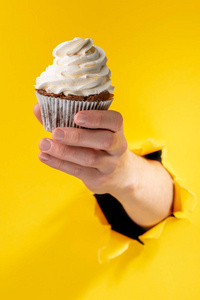 手拿着一个纸杯蛋糕穿过破烂的黄纸背景照片