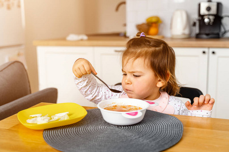 Baby toddler girl eats soup with spoon in her hand. 