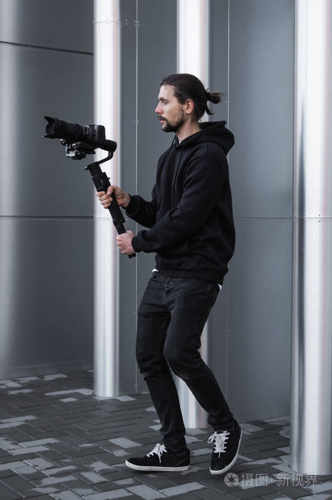 年轻的专业摄像师在3轴万向节稳定器上手持专业摄像机.