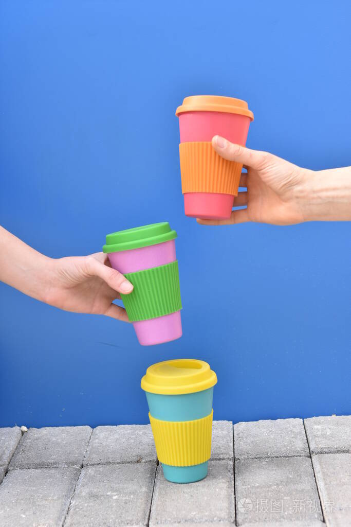 hands of two girls taking eco coffee cup on blue background, 