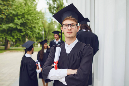 男毕业生在大学毕业生的背景下微笑着。