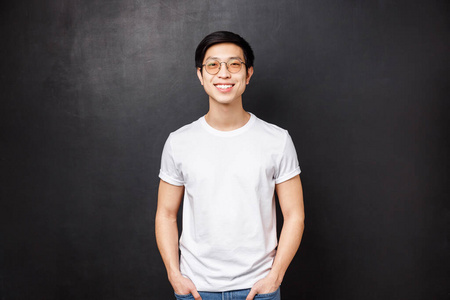 一位戴眼镜的亚洲年轻人的肖像，身穿白色休闲衬衫，黑色背景，友好微笑，表达快乐热情的情绪，大学毕业后与同学们一起悬挂