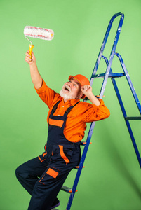 油漆工楼梯。修理。一个穿着工作服的人在空房间里粉刷墙壁。整体油漆工，盖上油漆桶。建筑工人粉刷立面。保温工程