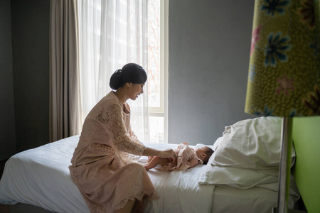 亚洲年轻妈妈穿着裙子在卧室里给宝宝换尿布照片