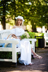 戴着帽子的年轻女子坐在木凳上，在公园里放松