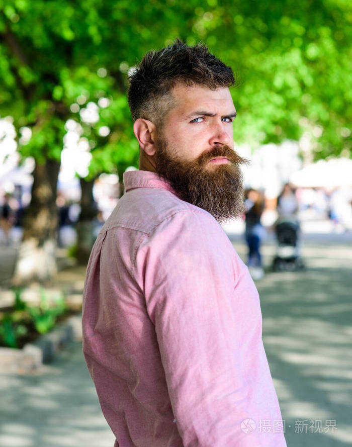 一个脸上留着胡子和胡子的男人在公园里散步时回头看了看理发师和发型