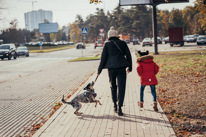 快乐的妈妈和女儿牵着狗在街上散步