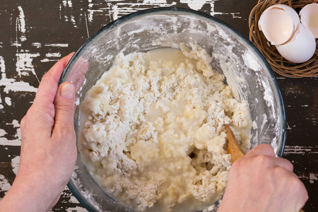 妇女手混合热水和面粉在棕色背景上用木勺做面团厨师