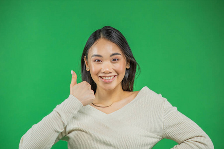 一位迷人的亚洲年轻女子在绿色背景上竖起大拇指