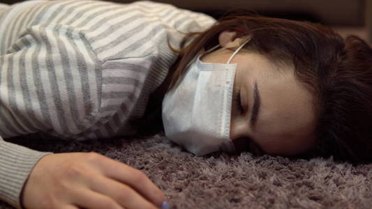 一个戴着医用面罩的女人躺在昏迷特写的地板上.照片