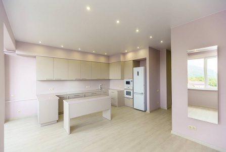 粉红色墙壁和白色厨房设备的大房间。厨房家具和所有厨房用具都是新的。厨房前面有一张白色的桌子。新的，新的装修。