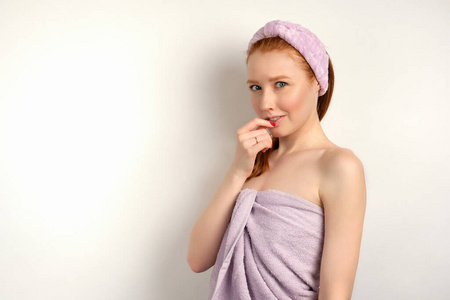 一位红发女孩,皮肤干净,裹着毛巾,头上缠着绷带,手指放在嘴唇上,狡猾