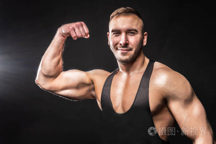 健美运动员穿着黑色衬衫在黑色背景上展示二头肌