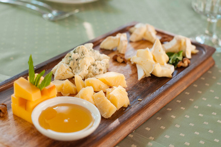 奶酪盘子。在木板上放蜂蜜的不同类型的奶酪。
