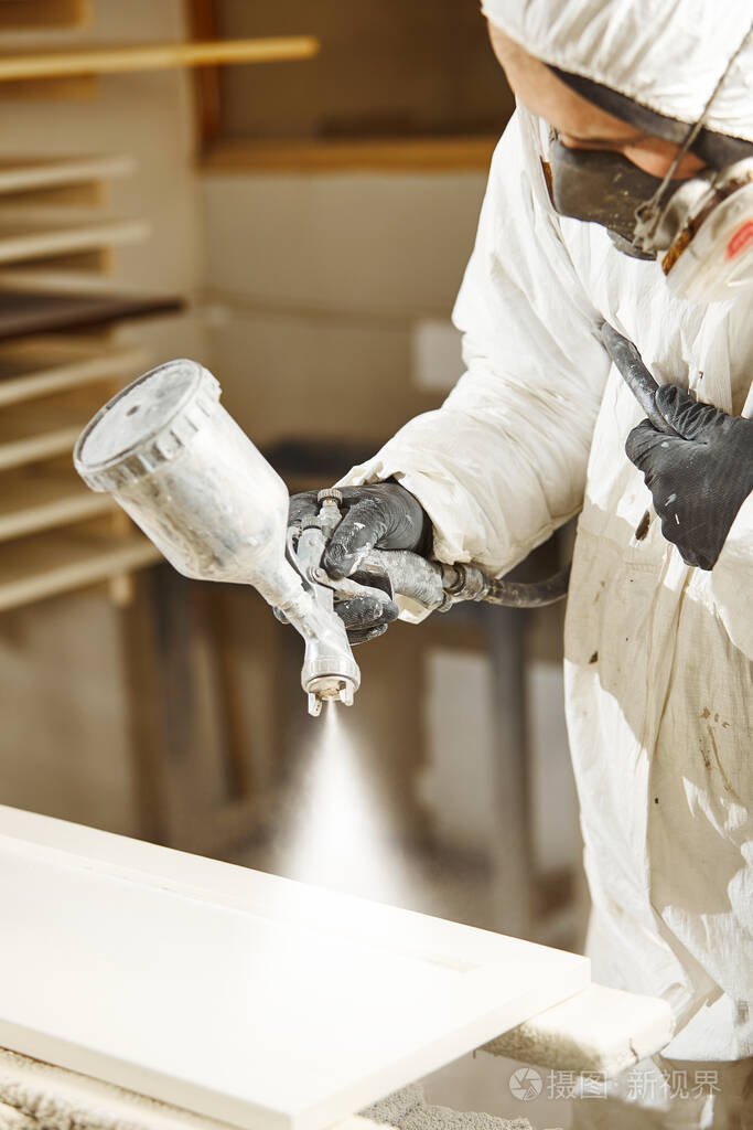 用喷漆枪对木材进行无空气喷涂的工人