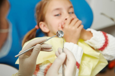 小女孩看起来很害怕,用医疗工具遮住牙医的嘴.照片