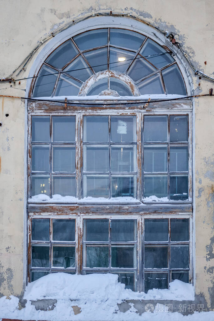 黄色墙上的一扇很大的拱形窗户上面有雪