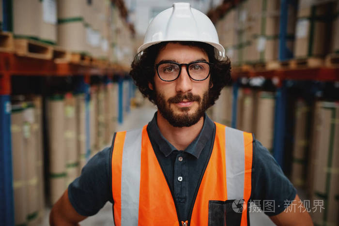 一幅自信的年轻白人工人的画像戴着白色安全帽穿着防护服戴着眼镜站在