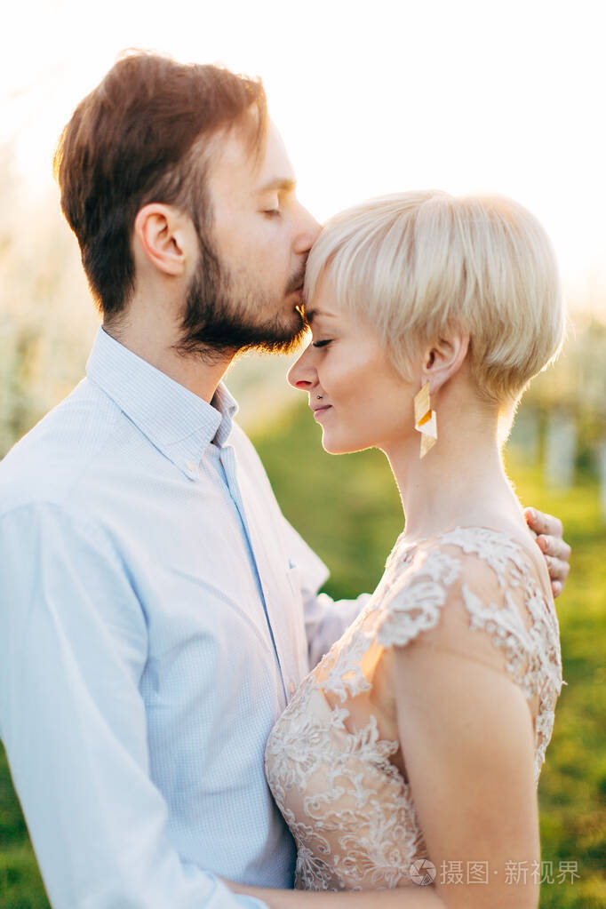 男人和女人站在春暖花开的公园或花园里,男人在亲吻他的女人的额头.