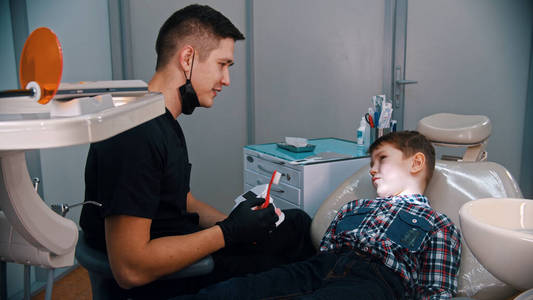一个正在接受现代牙科治疗的小男孩和微笑的医生谈论卫生和刷牙
