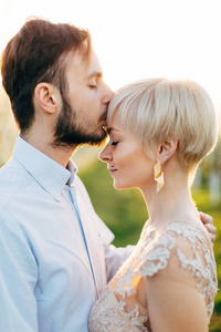 可爱的新婚夫妇穿着优雅的衣服拥抱着,男人亲吻着女人的额头.