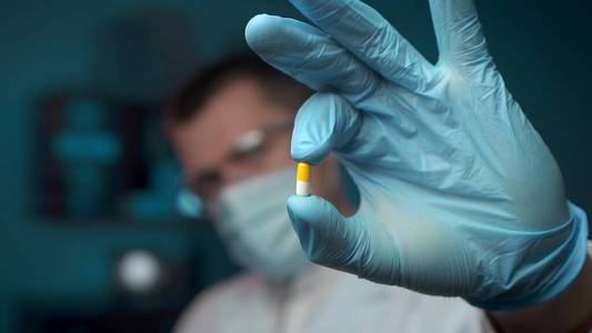 一位男性科学家在实验室分析一颗药丸的特写镜头