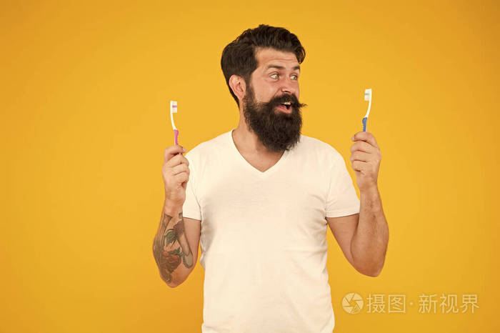 牙齿卫生。超声波洁牙技术。胡子男人拿着黄色背景的牙刷。这家伙拿着两把牙刷。时髦的笑脸关心卫生。刷牙概念