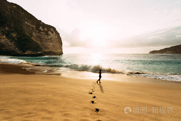 一个孤独的人站在海滩上.印度尼西亚,一名男子在海滩上与夕阳相遇.