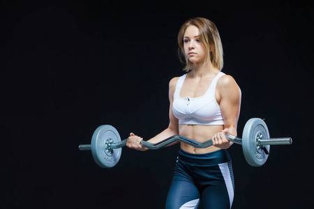 一个健身肌肉年轻女孩与卷曲杠铃摆在一个孤立的黑色背景上健身房的特写肖像