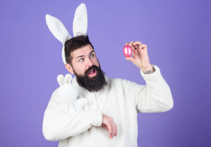男人帅气的脸戴着白色的兔子耳朵。复活节兔子。象征复活节的白色兔子。紫色背景上有玩具和复活节彩蛋的家伙。享受温柔。春节假期。当你是