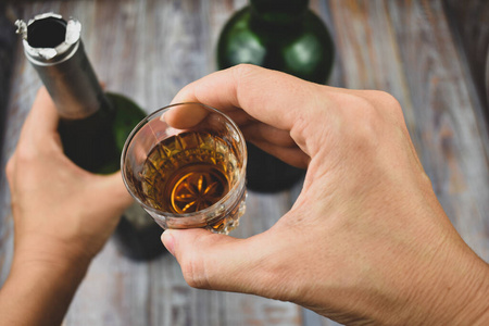 一个饮酒醉喝酒精饮料.手拿着一个玻璃杯和一瓶酒精.酗酒问题照片