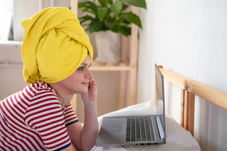 远程教育在线教育和工作。头上戴着黄毛巾的女人在床上远程办公。使用计算机