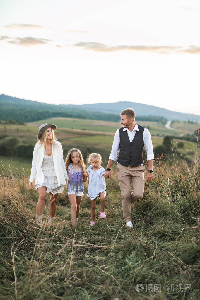 两个金发碧眼的小女儿牵着父母的手在大自然的夏日田野上妈妈爸爸和小
