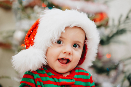 portrait of baby boy in Santa hat on Christmas tree light backgr