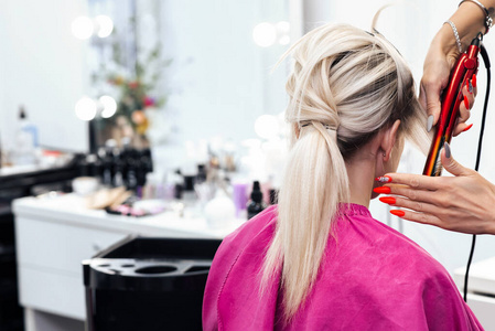 烫头发金发女孩由发型师用熨斗烫头发照片