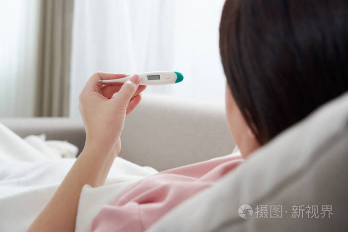 女人看着温度计女性手拿着数字温度计发烧烟道或病毒的概念