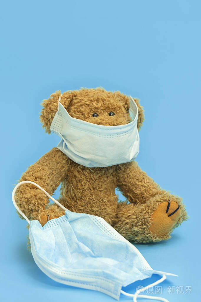 棕色泰迪熊戴着面罩手臂上夹着一个面具背景是蓝色有复印空间