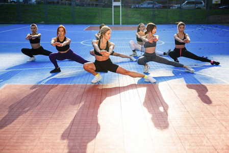 一群穿着运动服的迷人的年轻运动女孩在绿色公园的运动场上做着深蹲