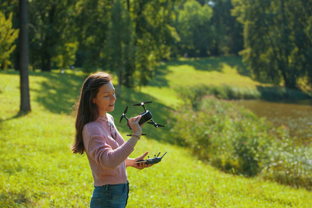 公园空地上的一位年轻女子发射了一架无人机，一手拿着飞机，一手拿着控制面板。