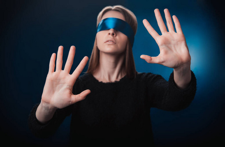 女孩蒙着眼睛,带着蓝丝带,用手找东西,在蓝色背景上玩耍,娱乐照片