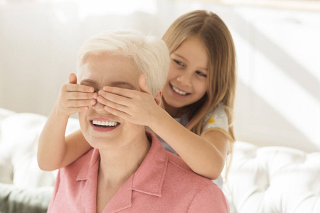 快乐的小女孩从后面闭上祖母的眼睛，在家里给她惊喜