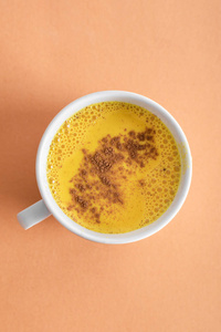 白色的金色牛奶杯，有姜黄和肉桂粉，在浅腌料的背景下。闭合。喝一杯能增强健康免疫力的饮料。