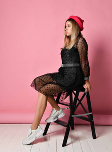 她坐在梯子上,在粉红色的背景上侧身摆姿势.全长照片