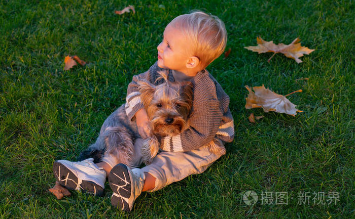 可爱的小孩抚摸着他的小狗,坐在绿草丛中.