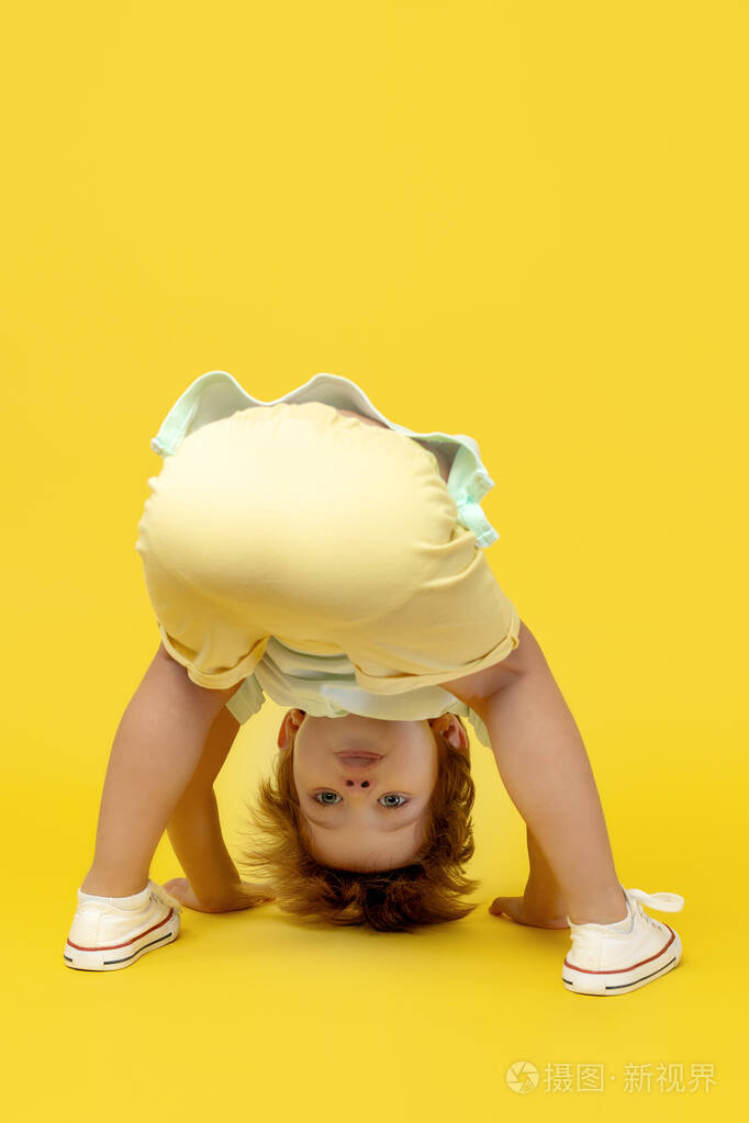 有趣的孩子在黄色背景上倒立着玩