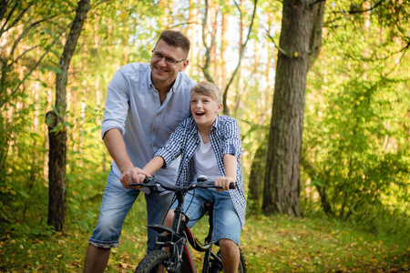 年轻的父亲教他微笑的儿子如何骑自行车