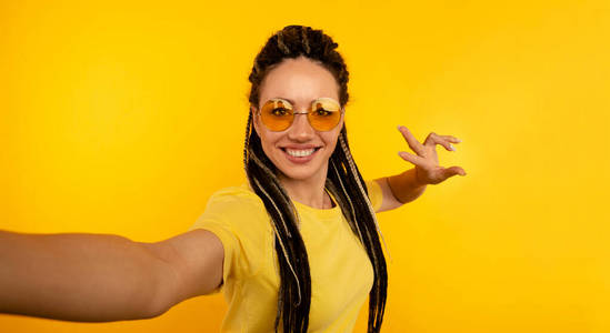 戴着墨镜的欢快的女人在黄色的摄影棚里自拍。