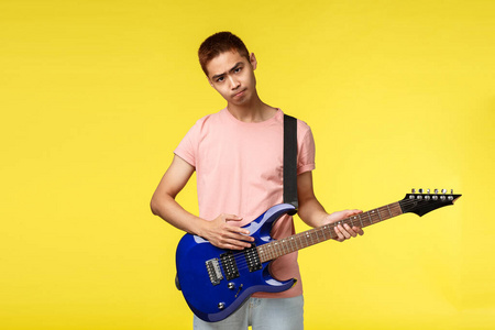 年轻英俊的音乐家弹吉他唱歌，在黄色背景下与世隔绝